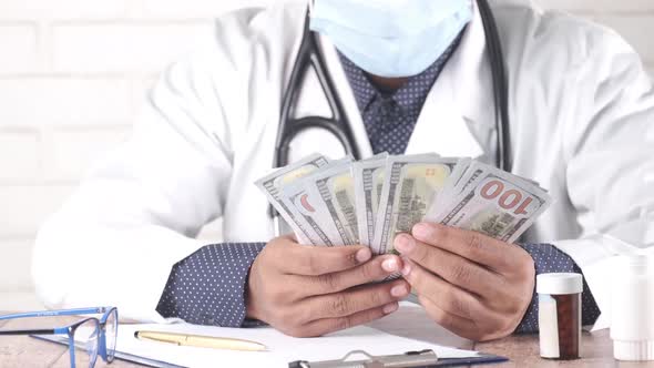 Doctor Counting 100 Us Dollar Cash on Clinic Desk alt
