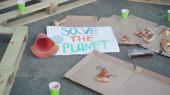 Save the Planet Banner Lying on Asphalt with Garbage Around. Half-eaten Pizza and Empty Plastic Cups alt