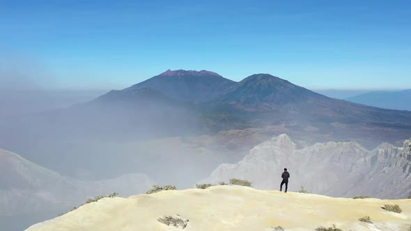 Dolly Zoom Aerial view of a traveler standing on the edge of a cliff at the crater of a mountain