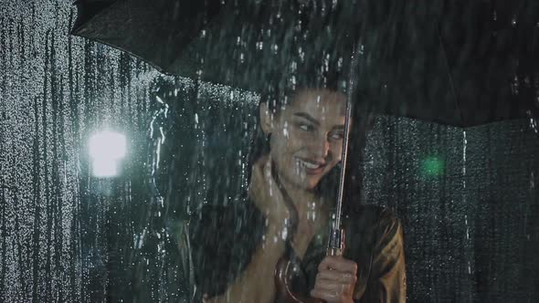 Flirting Look at Camera of Happy Girl with Umbrella Under Night Heavy Rain alt