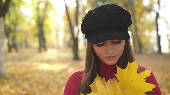 Portrait of Girl with Maple Leaves Looks at the Sky and Poses at Camera in Park alt
