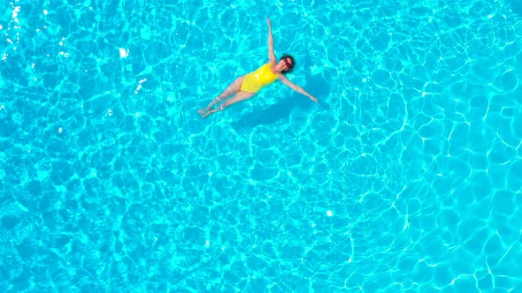 View From the Top As a Woman in a Yellow Swimsuit Lying on Her Back in the Pool alt