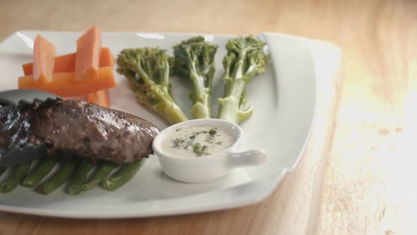 Slider Shot of a Square Plate With Vegetable on it Then the Serving of Steak Next to the Sauce Pot o alt