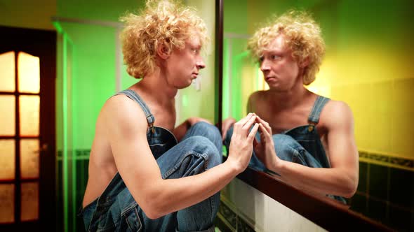 Side View of Angry Androgynous Man Touching and Hitting Mirror Looking at Reflection alt