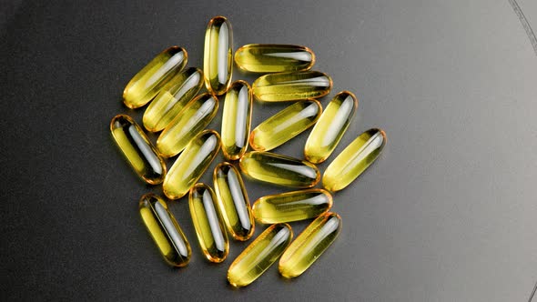 Group of Golden Transparent Pills with Liquid Medicine Rotating on Black Surface