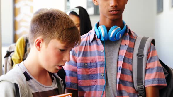 Students standing with notebook and digital tablet in corridor alt