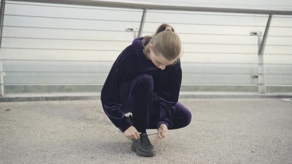 Wide Shot of Young Caucasian Sportswoman Tying Shoelaces and Leaving alt