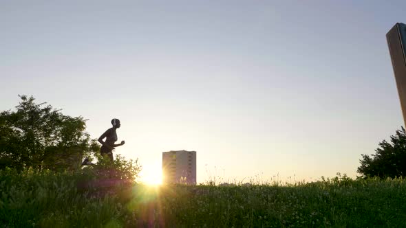 Slow motion shot of woman with headphones jogging on meadow at sunset alt