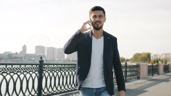 Handsome Mixed Race Guy Walking in River Embankment and Talking on Mobile Phone alt