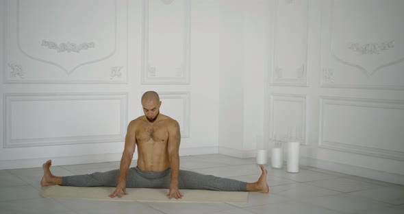 Male Yogi Is Sitting in Split Position in Hall and Meditating with Closed Eyes alt