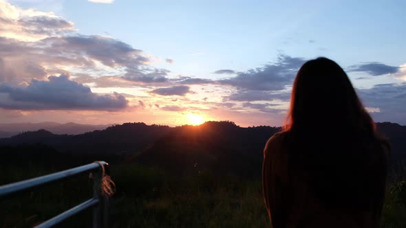 Silhouette rear view of a woman watching sunset sky on the mountain peak