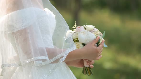 A bride in a white dress is holding a pastel-colored wedding bouquet. Hand close-up