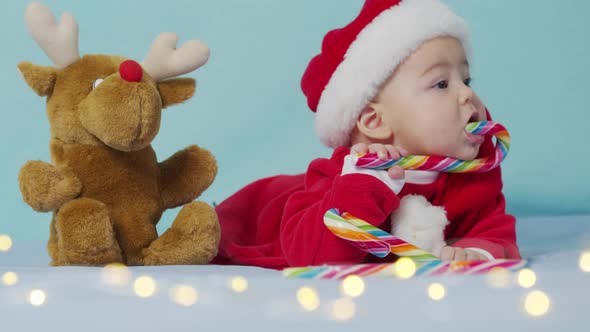 Smiling Funny Newborn Baby in Santa Claus Hat Red Bodysuit Play on White Soft Bed Lick Sweet alt