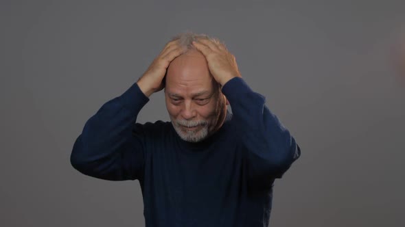 Depressed Man in Blue Pullover Runs Hands on Grey Hair alt