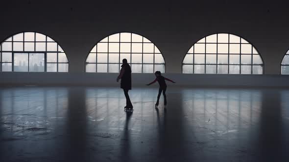 Woman Coach and Student Little Girl Skating on Dark Ice Arena alt