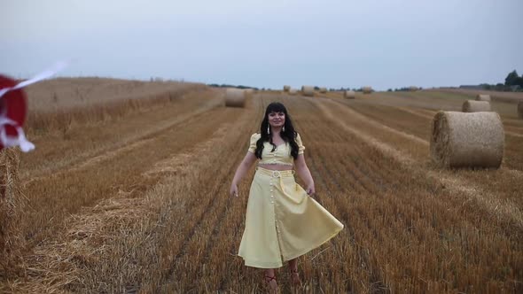 A Beautiful Sweet Brunette Woman in a Field with Hay on a Haystack in a Yellow Stylish Dress