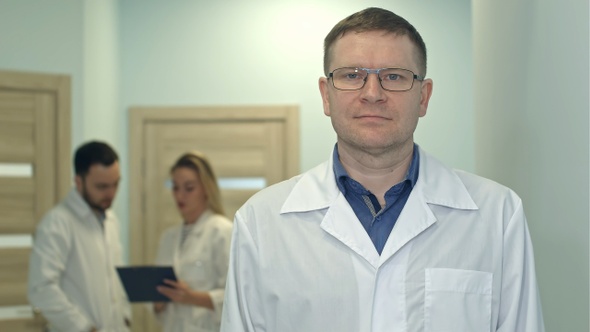 Male doctor looking at camera while medical staff working
