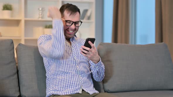 Excited Man Celebrating Success on Smartphone at Home  alt