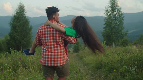 Romantic Black Man Carrying Excited Asian Woman in Arms and Whirling on Mountain Hill alt