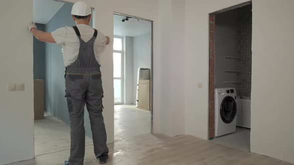 A Builder in Working Uniform Checks the Size and Quality of Doorways in a New Apartment alt