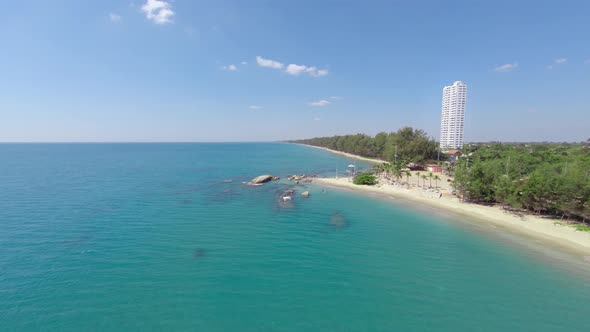 Aerial, seascape view of the coastline in Rayong called Mae Ramphueng beach with a tall white hotel alt