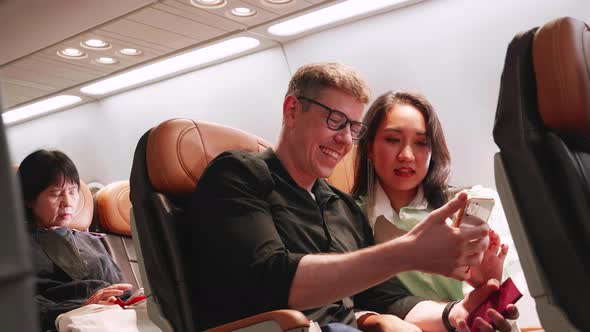 young couple in love traveling in airplane see smartphones and smile together on the airplane