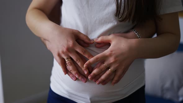 Loving Young Husband and Wife Make Heart Sign Hugging Pregnant Belly alt
