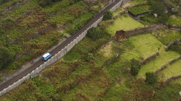 Aerial of a VW-Camper van from far away driving up a hill on Madeira alt