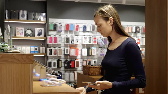 Young Woman Chooses a New Smartphone in an Electronics Store