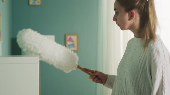 Pretty Lady in White Sweater Wipes Dust From Furniture alt