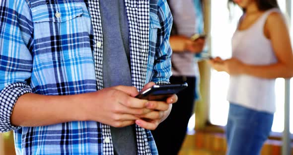 Mid-section of boy using mobile phone in corridor alt