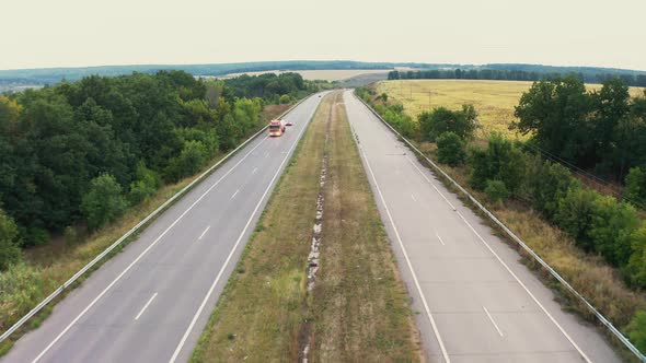 Cars Drive on One Lane of Long Road Stretching Between Trees