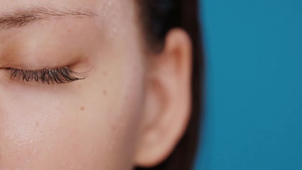 Close-up of Closed Woman Eye with Brown Long Eyelashes and Wet Skin on Blue Background alt