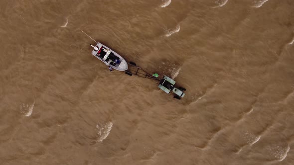 Tractor attached to boat in shallow water, top down aerial view alt