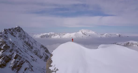 Aerial drone view of a mountain climber skier on the peak summit top of a snow covered mountain alt