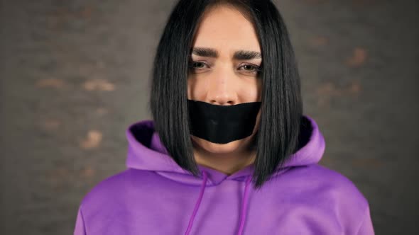 Sad Crying Young Woman Showing Emotions with Her Mouth Covered in Duct Tape alt