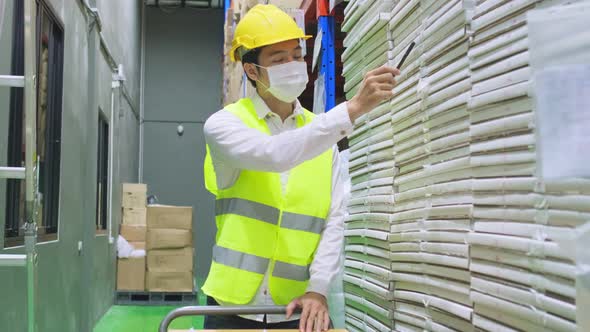 Asian male engineer worker wear mask working during covid pandemic in store warehouse shipping. alt