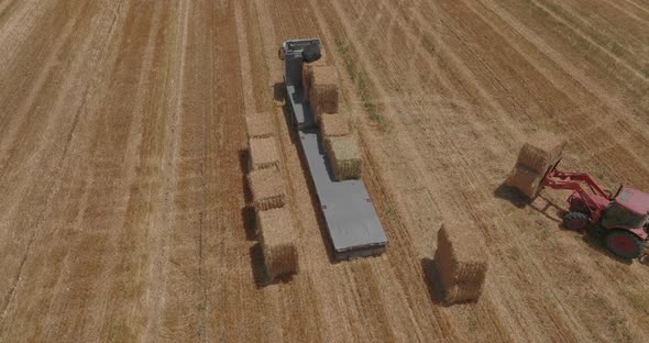 Red tractor loading Hay bales onto a parked truck, Aerial footage. alt