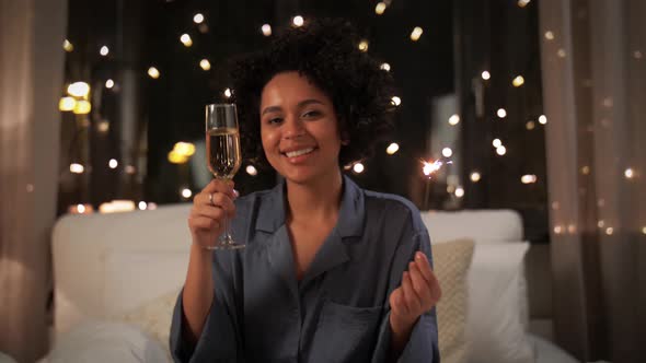 Happy Woman Drinking Champagne in Bed at Night