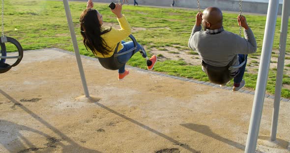 Rear view of couple playing on playground swing in the park 4k alt