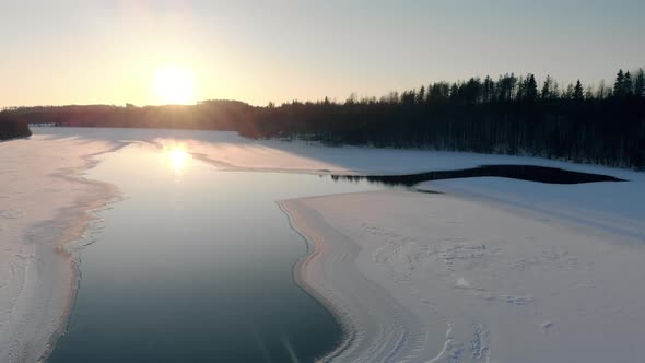 Frozen river in the middle of a forest in an aerial view at sunrise alt