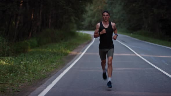 Athlete in a Sports Uniform Runs Along an Asphalt Road Track in the Forest