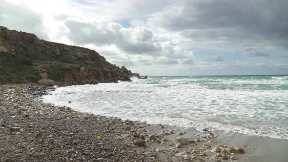 Piles of Rocks On a Golden Bay Beach with Mediterranean Sea Waves Crashing on Sandy Shore alt