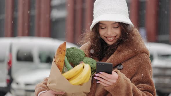 A Woman is Standing Near a Supermarket and Texting on a Smartphone alt