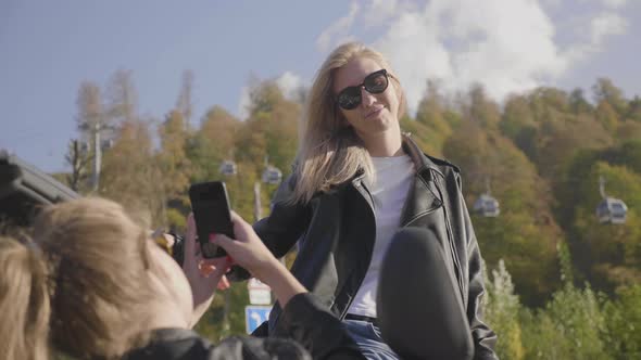 Two Caucasian Girls in a Cabriolet are Photographed on the Phone and Smiling