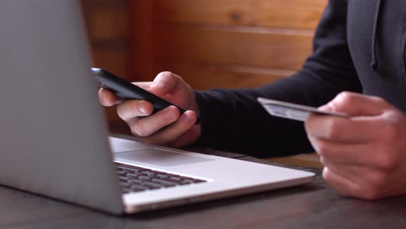 Businessman in a Black Hoodie Making Online Payment with Credit Card and Smartphone, Online Shopping alt