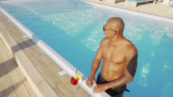 Handsome African Man Enjoying Drinking Cocktail in the Swimming Pool