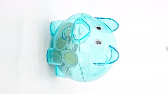 Hand is putting a coin or money in a piggy bank on white background, Vertical video format. alt