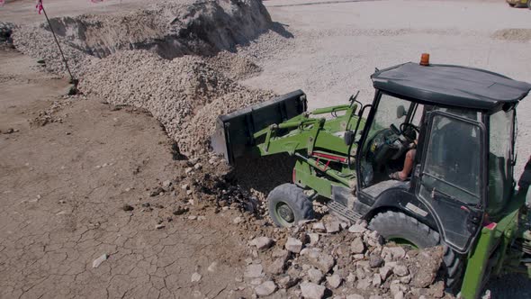 Green Construction Tractor That Loads the Stone From One Mound and Transports the Stone Elsewhere alt
