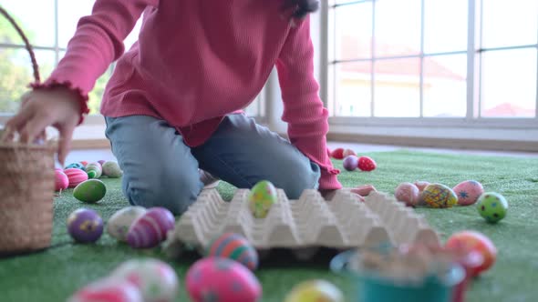 Asian little girl put green Easter eggs into the panel and enjoy for Easter celebration in her home alt